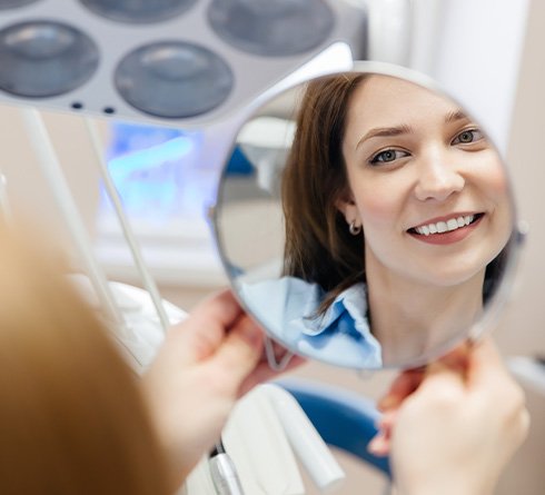 Happy dental patient looking at her teeth in mirror